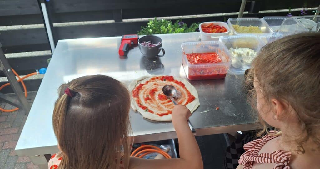 Kinderen beleggen zelfgemaakte pizza’s aan een feestelijk versierde tafel tijdens een pizza party.